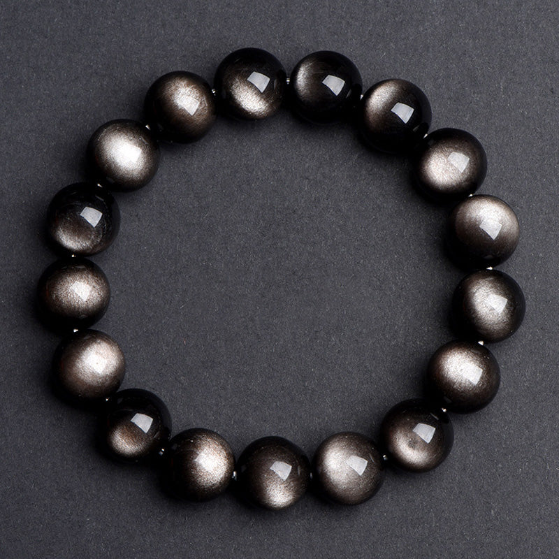 A silver sheen obsidian bracelet placed on a gray background, with noticeable contrast between black beads and silver luster.