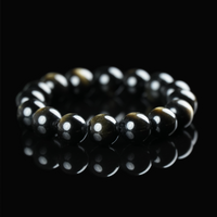 A close-up of a silver sheen obsidian bracelet resting on a black reflective surface, highlighting its deep tone and subtle sheen.