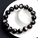A silver sheen obsidian bracelet coiled on white porcelain, reflecting soft light from its surface.