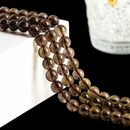 Strands of glossy smoky quartz round beads hang naturally over a white geometric display block. The beads are semi-transparent with warm, earthy tones, and their reflections add a sense of depth and shine.