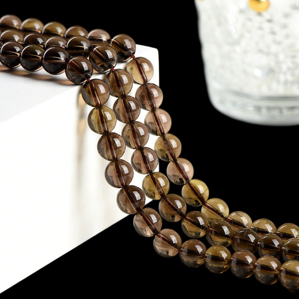 Strands of glossy smoky quartz round beads hang naturally over a white geometric display block. The beads are semi-transparent with warm, earthy tones, and their reflections add a sense of depth and shine.