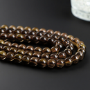 This image features several strands of natural smoky quartz beads arranged in a coiled formation on a matte black background. The beads vary slightly in tone from golden brown to deep smoky gray, enhancing their organic appeal.