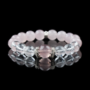 A close-up of a beaded bracelet made of strawberry quartz, rose quartz, and clear quartz, accented with silver-toned spacers. The bracelet lies on a glossy black surface, highlighting the crystals’ smooth polish and gentle pink tones.
