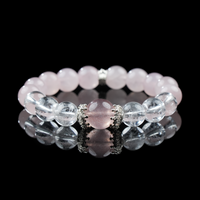 A close-up of a beaded bracelet made of strawberry quartz, rose quartz, and clear quartz, accented with silver-toned spacers. The bracelet lies on a glossy black surface, highlighting the crystals’ smooth polish and gentle pink tones.