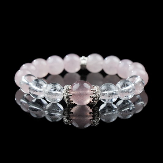 A close-up of a beaded bracelet made of strawberry quartz, rose quartz, and clear quartz, accented with silver-toned spacers. The bracelet lies on a glossy black surface, highlighting the crystals’ smooth polish and gentle pink tones.
