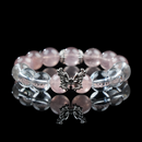 A handcrafted bracelet made of strawberry quartz and white phantom quartz beads, featuring a silver butterfly charm at the center, displayed on a reflective black surface.