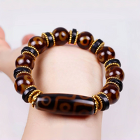 The bracelet is worn around a wrist, offering a clear view of how it looks when worn. The central Dzi bead sits prominently at the top, while the polished brown agate beads and gold-accented black spacers encircle the wrist. The image highlights the bracelet’s flexibility, rich tones, and bold spiritual design.