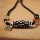 A photo of a Tibetan 9-Eye Dzi Agate necklace on a black background, showcasing the beadwork, jade, and gold details.
