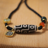 A photo of a Tibetan 9-Eye Dzi Agate necklace on a black background, showcasing the beadwork, jade, and gold details.