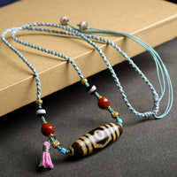 A close-up image of the Tibetan Agate Three-Eyed Dzi Bead Necklace displayed against a dark background, highlighting the intricate design and vibrant beads.