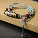 The Tibetan Agate Three-Eyed Dzi Bead Necklace placed flat on a textured surface, with the unique pattern of beads clearly visible, giving an elegant and vintage feel.