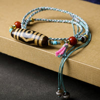 The Tibetan Agate Three-Eyed Dzi Bead Necklace placed flat on a textured surface, with the unique pattern of beads clearly visible, giving an elegant and vintage feel.