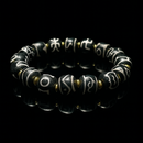 A high-contrast luxury presentation of a Tibetan-style Dzi bead bracelet laid on a glossy black mirror background. The reflection enhances the deep black tones of the beads, which are etched with intricate white script. Gold-tone spacers add a touch of elegance, making this a visually striking and spiritually meaningful accessory.
