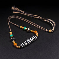 A handcrafted Tibetan Nine-Eye Agate Dzi bead necklace featuring turquoise, black agate, and golden spacers, displayed against a black backdrop for emphasis on the intricate design.