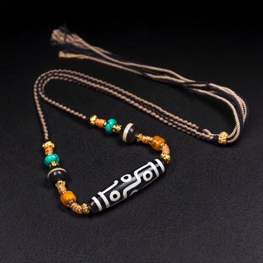 A handcrafted Tibetan Nine-Eye Agate Dzi bead necklace featuring turquoise, black agate, and golden spacers, displayed against a black backdrop for emphasis on the intricate design.