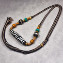 A close-up of the Tibetan Nine-Eye Agate Dzi bead necklace held in a hand, highlighting the adjustable cord and colorful beads along with the large Dzi bead at the center.