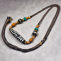 A close-up of the Tibetan Nine-Eye Agate Dzi bead necklace held in a hand, highlighting the adjustable cord and colorful beads along with the large Dzi bead at the center.