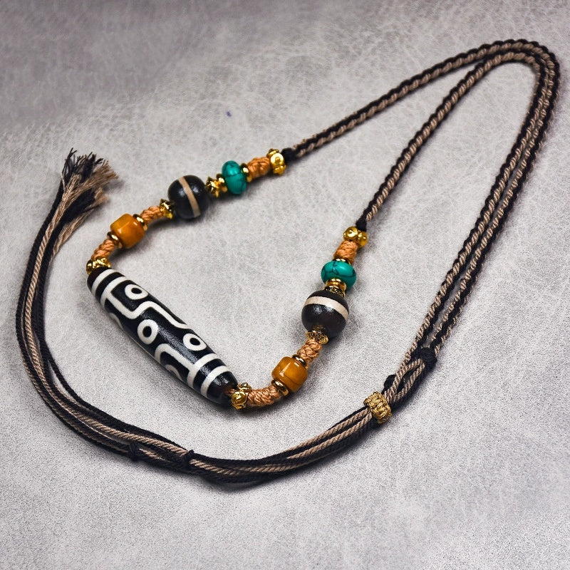 A close-up of the Tibetan Nine-Eye Agate Dzi bead necklace held in a hand, highlighting the adjustable cord and colorful beads along with the large Dzi bead at the center.