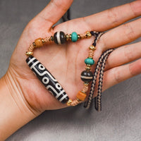 The Tibetan Nine-Eye Agate Dzi bead necklace featuring vibrant turquoise, black agate, and gold spacers, laid on a textured gray surface, showcasing its intricate craftsmanship.