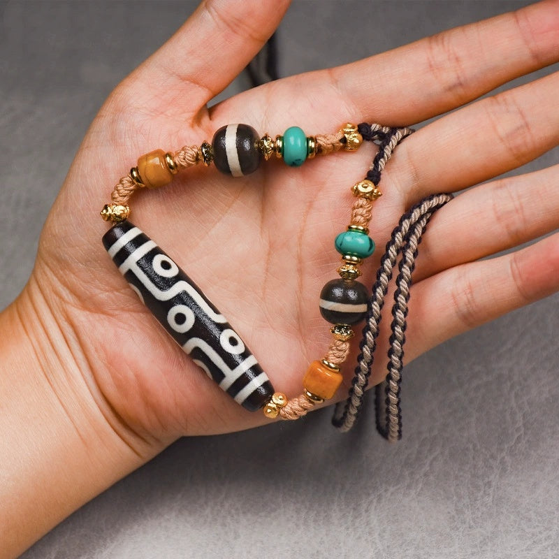 The Tibetan Nine-Eye Agate Dzi bead necklace featuring vibrant turquoise, black agate, and gold spacers, laid on a textured gray surface, showcasing its intricate craftsmanship.