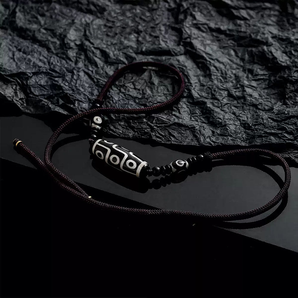 The Tibetan Nine-Eyed Dzi bead necklace is placed on a textured, crumpled black background, emphasizing the traditional craftsmanship of the beads.