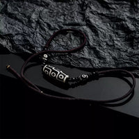 The Tibetan Nine-Eyed Dzi bead necklace is placed on a textured, crumpled black background, emphasizing the traditional craftsmanship of the beads.