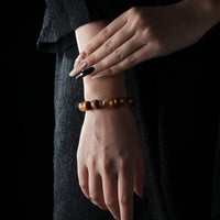 Elegant bracelet made of polished Tiger’s Eye, Citrine & Clear Quartz Bracelet，worn on a wrist against a black textured dress background.