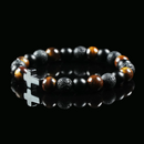 Bracelet made of tiger’s eye, lava stone, and obsidian beads with a silver cross charm, displayed on a black background to emphasize its earthy power and balance.
