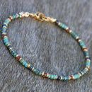 A turquoise beaded anklet with golden clasp laid flat on a gray wood surface.
