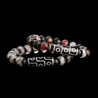 A pair of vintage-style Tibetan bracelets featuring classic black and white 9-eye Dzi beads. The surrounding round beads come in a weathered palette of red, gray, and black, creating a rustic, well-worn aesthetic. Shot on a black background to emphasize the traditional craftsmanship.