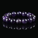 A close-up of a Uruguayan amethyst bracelet with rich, deep purple beads resting on a black reflective surface.