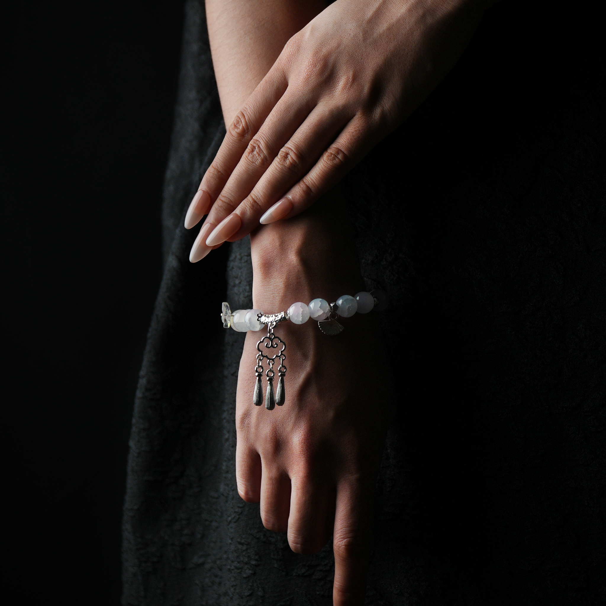 A graceful wrist adorned with a glowing energy bead bracelet featuring a silver Xiangyun (auspicious cloud) charm and dangling tassels, embodying peace, culture, and spiritual alignment.