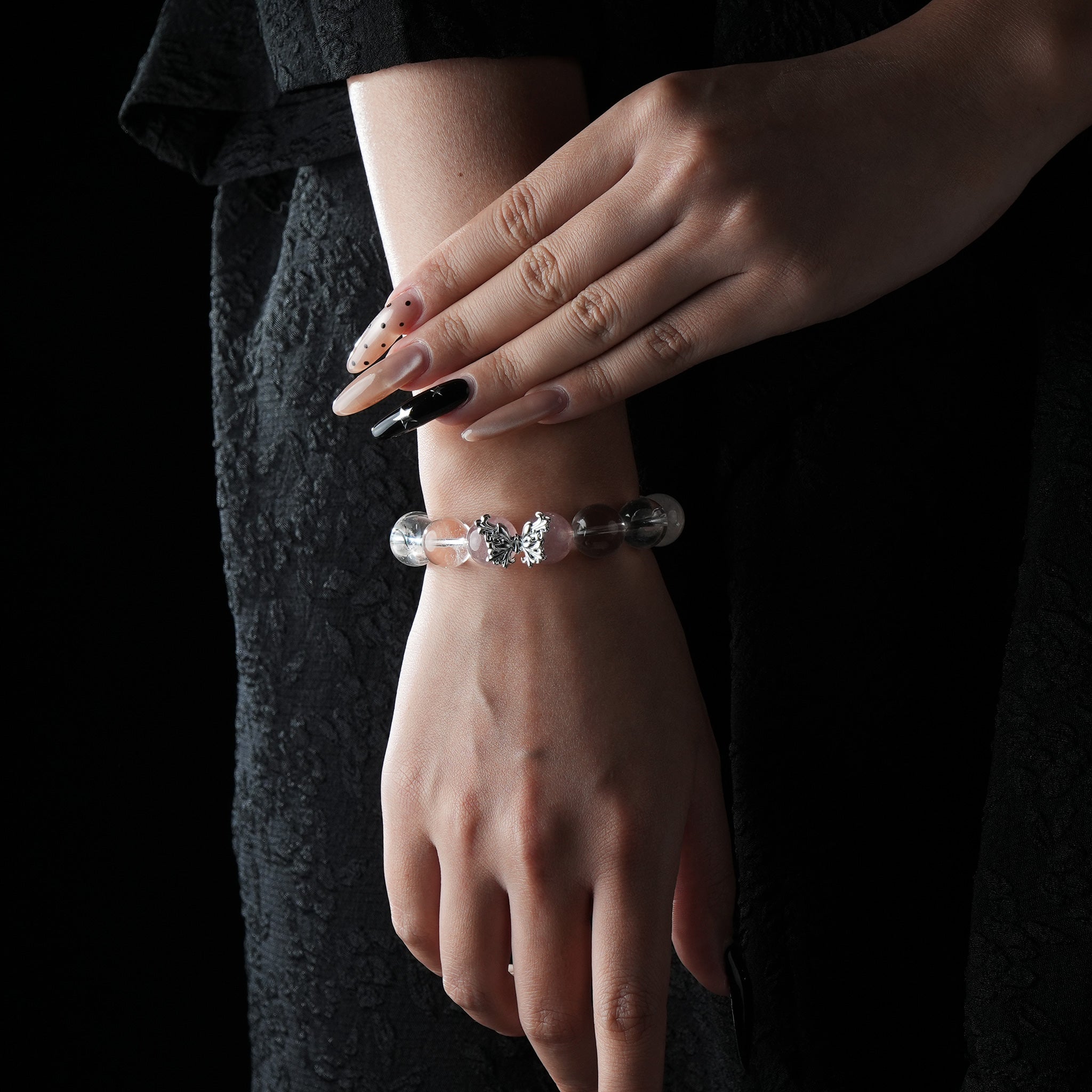 A stylish bracelet made of strawberry quartz and clear quartz beads with a silver butterfly charm, elegantly worn on the wrist.