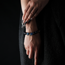 Woman wearing a bracelet made of aquamarine, blue sandstone, and moonstone with a small gold charm, against a dark outfit.