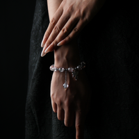 A wrist wearing a clear and blush-toned energy bead bracelet—delicate and luminous, with a butterfly charm that dances like a tiny fairy, enhancing its soft elegance.