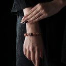 A red hematoid quartz crystal bracelet with warm reddish tones is worn on the wrist, styled against a black outfit to highlight the natural gemstone's color and polish.