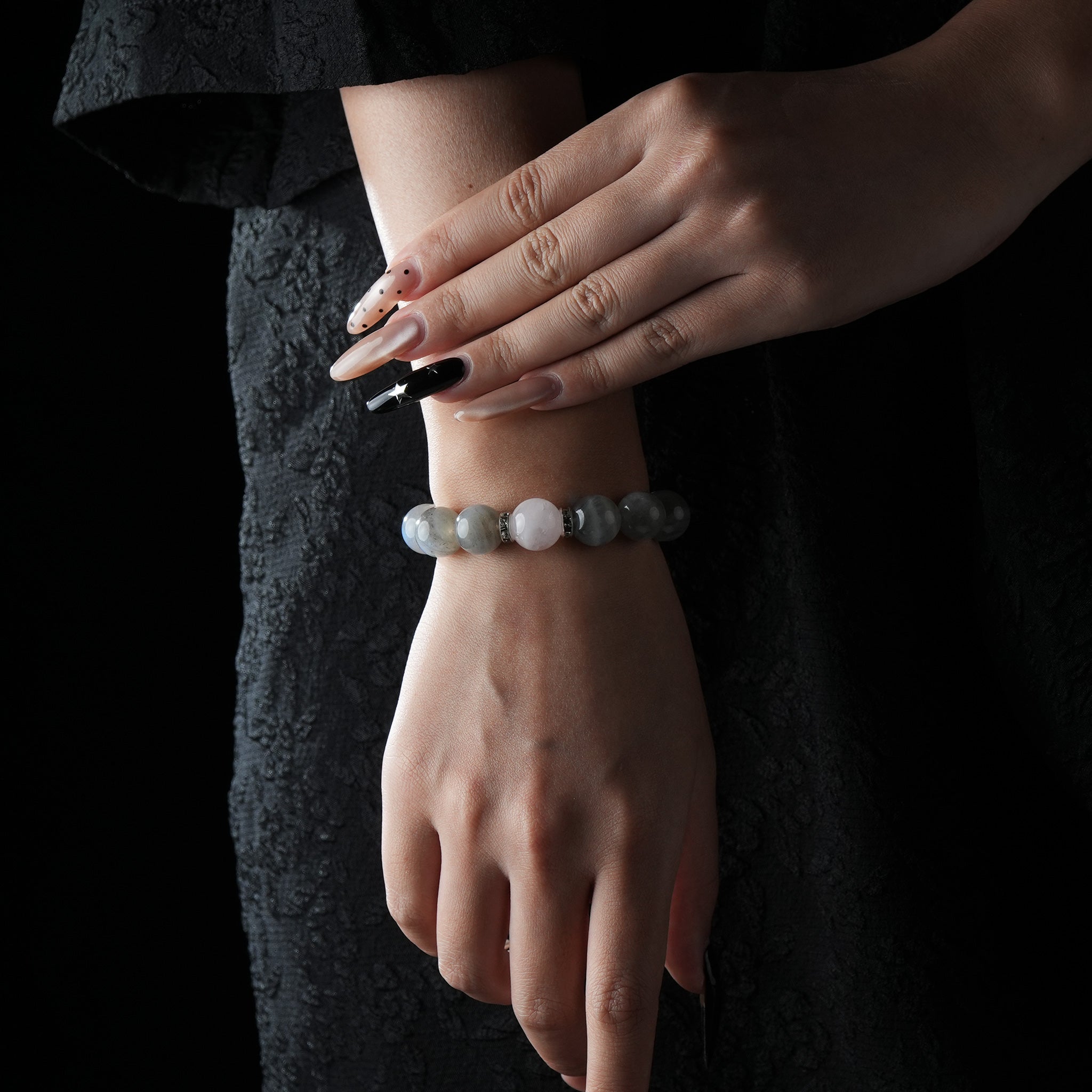 A person wearing a rose quartz and gray moonstone bracelet, styled with a black outfit to highlight the calming colors and elegant stone arrangement.