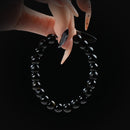 Black obsidian beaded bracelet combining matte and glossy textures, held by hand on black background for protection and grounding.