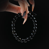 Black obsidian beaded bracelet combining matte and glossy textures, held by hand on black background for protection and grounding.