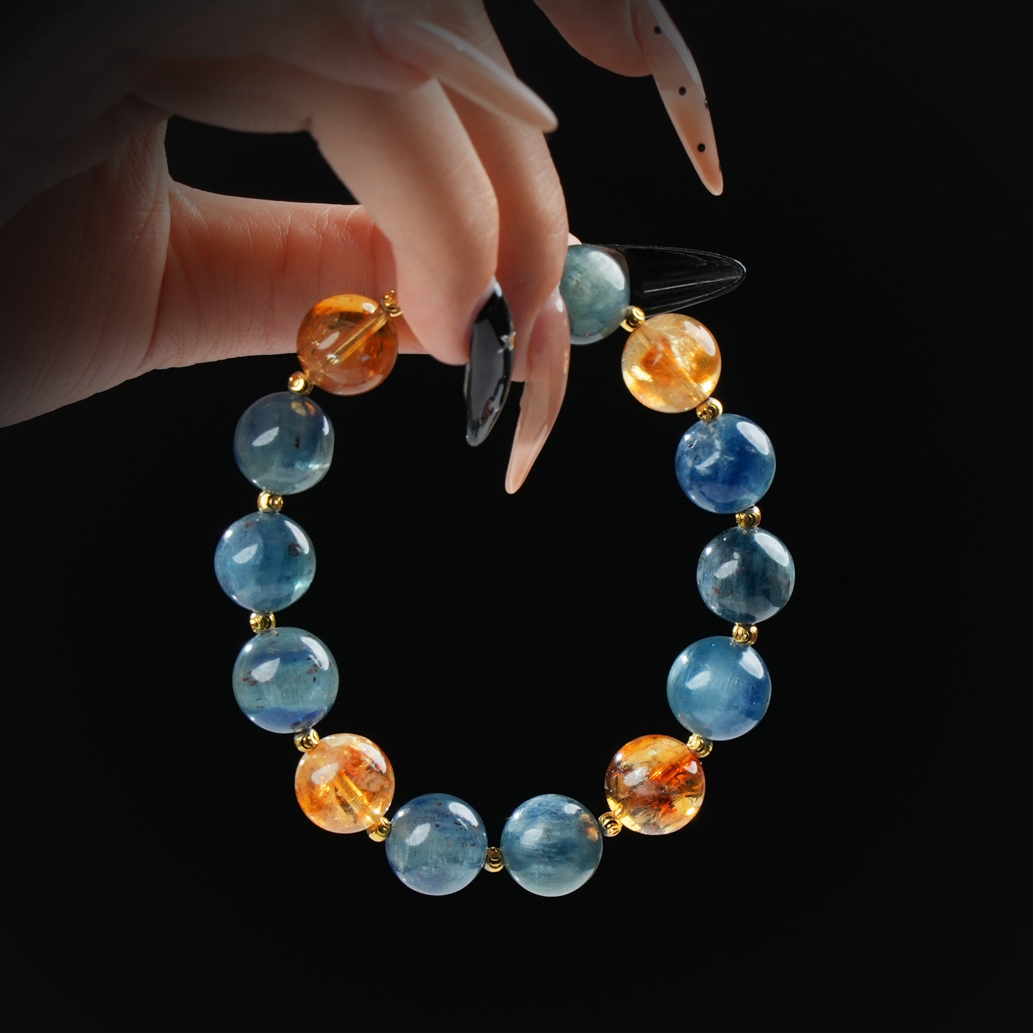 Blue kyanite and citrine beaded bracelet with gold spacers, held by hand on black background for clarity and energy.