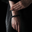 Elegant bracelet made of polished blue tiger eye beads, worn on the wrist against a dark textured background.