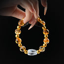 Citrine and clear quartz beaded bracelet with matte gold spacers and raw quartz centerpiece, held by hand on black background for prosperity and energy.