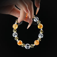 Citrine, golden rutile, and clear quartz beaded bracelet held by hand on black background for abundance and energy amplification.