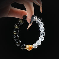 Gold obsidian, citrine, and clear quartz beaded bracelet held by hand against a black background for a bold and energetic look.