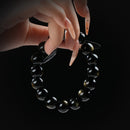 Golden obsidian beaded bracelet with subtle shimmer, held by hand on black background for grounding and protection.