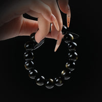 Golden obsidian beaded bracelet with subtle shimmer, held by hand on black background for grounding and protection.