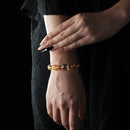 Bracelet made of golden rutilated quartz, citrine, and clear quartz beads, glowing with warm golden tones, worn on a wrist against a black textured background.