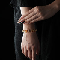Bracelet made of golden rutilated quartz, citrine, and clear quartz beads, glowing with warm golden tones, worn on a wrist against a black textured background.