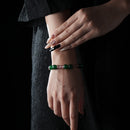 Elegant bracelet with alternating green jade and rose quartz beads, worn on a wrist against a dark textured fabric background.