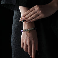 Bracelet made of labradorite and amethyst beads with a gold star charm, worn on the wrist against a black lace dress background.